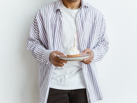 Person holding a cupcake with a lit candle, wearing a striped shirt. Celebrate special moments.