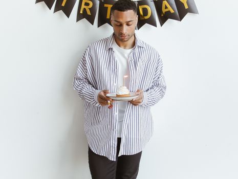Young man in striped shirt holding cupcake with candle under birthday banner.