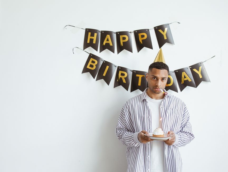 Jovem celebrando sozinho com bolo e chapéu de festa, ambiente interno de aniversário