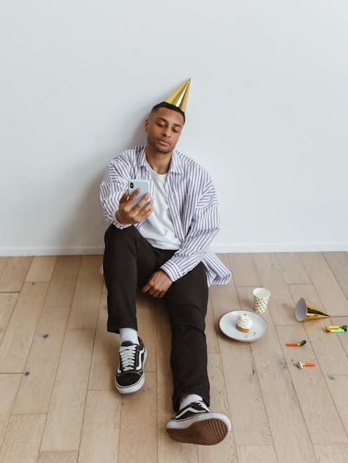 Man in Party Hat Sitting with Smartphone
