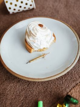 Close-up of a cream tart with a decorative candle on a plate, shot in a vertical composition.