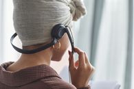 Back view of crop anonymous female call agent with microphone in turban standing in light room during work at home