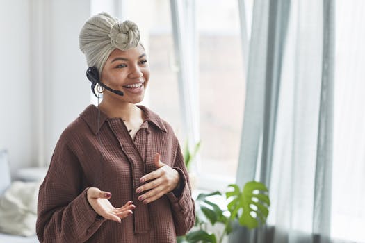 Cheerful woman with a headset and turban speaking indoors near a window.