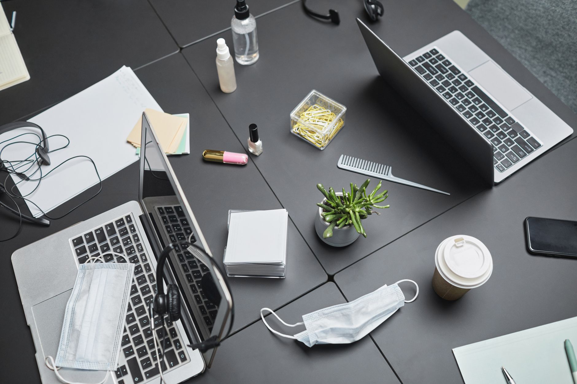 Top view of a modern office desk with laptops, masks, and office supplies, highlighting a safe workspace.