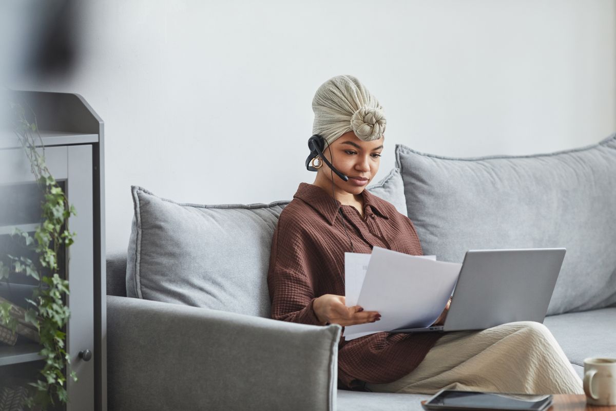 African American woman reviewing documents while working with a laptop at home