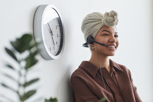 Free Cheerful black operator with headset sitting at wall Stock Photo