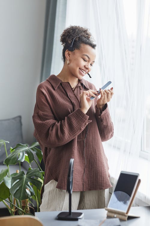 Cheerful black woman in headset filing nails