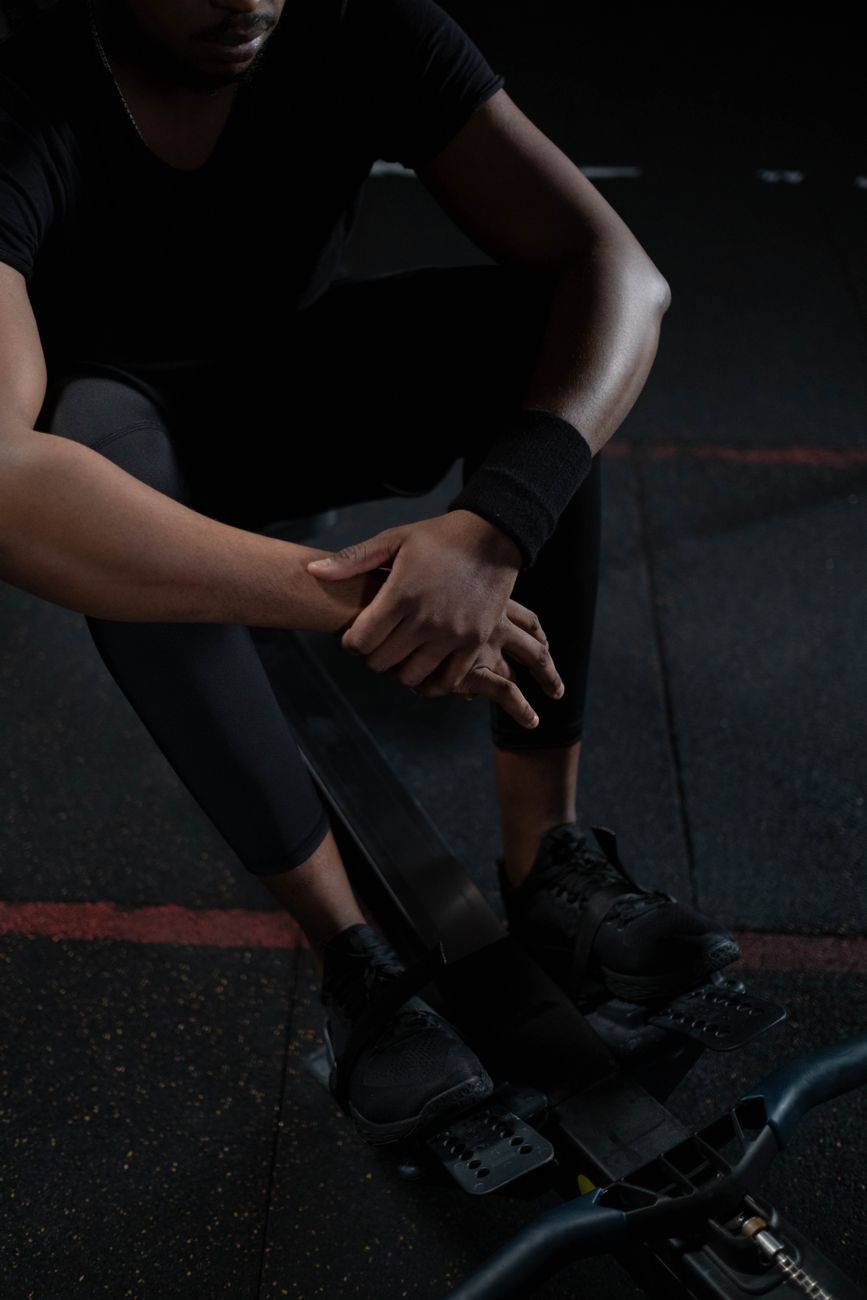 A man in sportswear resting on a rowing machine in a dimly lit gym setting.