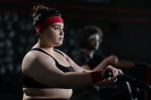 Free Determined woman in gym wear exercising on a stationary bike, exemplifying body positivity and fitness. Stock Photo