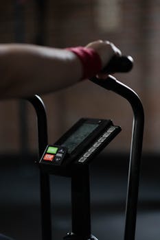 Person holding exercise bike handlebar, focused on equipment display, indoor gym setting.