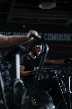 Fit man smiles while working out on a stationary bike in an indoor gym.