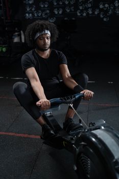 Focused young man using rowing machine for workout at an indoor gym, promoting fitness and well-being.