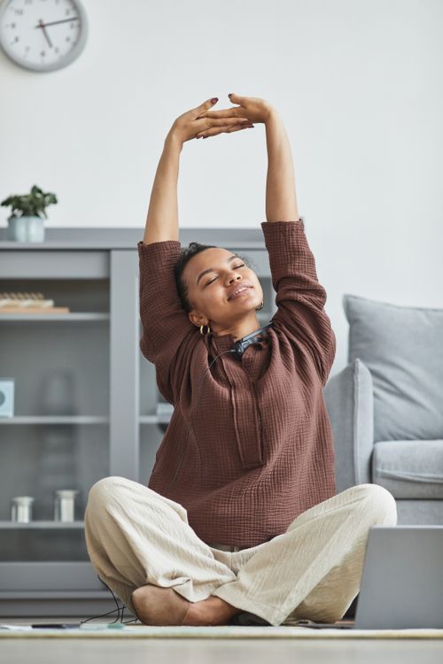 Free African American woman stretching in a cozy living room, enjoying a moment of relaxation. Stock Photo