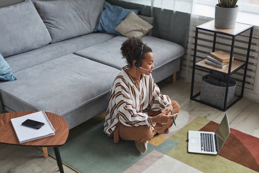 African American woman working remotely at home, sitting on the floor with laptop and headset.