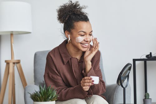 Smiling Woman in Shirt Sitting and Applying Cream