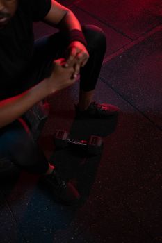 High-angle view of a man resting in a gym beside a dumbbell under red lighting.