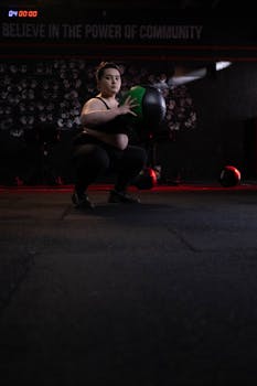 Woman performing squat with a medicine ball indoors, showcasing strength and focus.