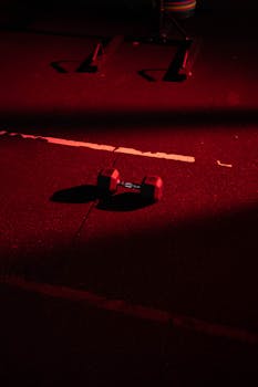 A single dumbbell on a gym floor, dramatically lit with red lighting.