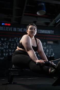 Confident plus-size woman working out on a rowing machine in a well-equipped gym.
