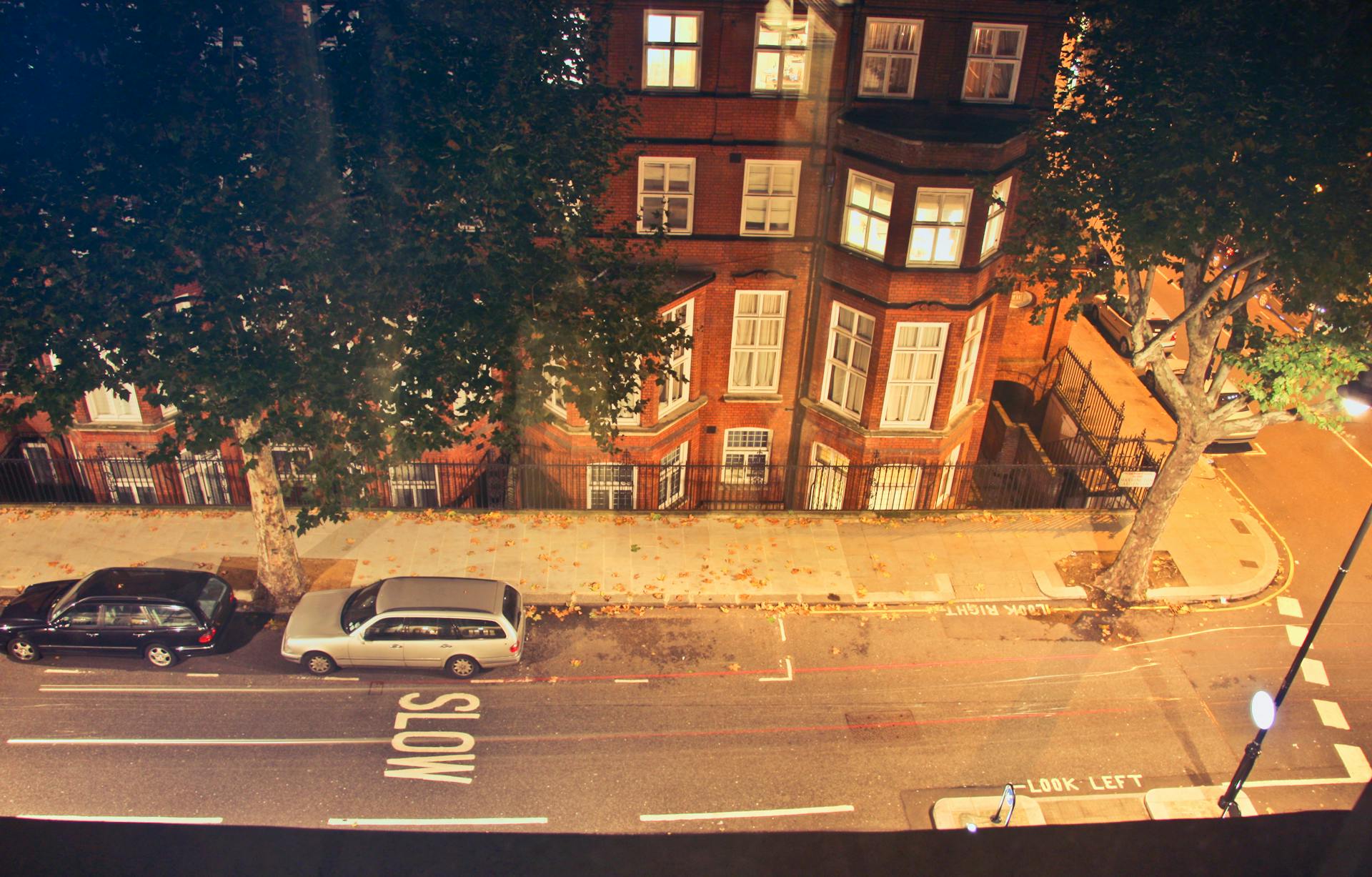 Aerial shot of a London street scene at night featuring parked cars and classic architecture.