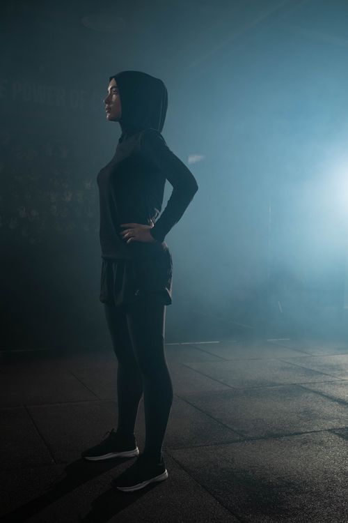 Free A Muslim woman in a hijab stretching indoors in a gym with a smoky background, highlighting fitness and wellness. Stock Photo