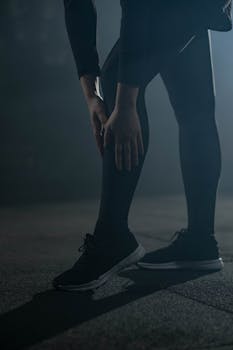 Silhouette of an athlete stretching in dark gym, highlighting activewear and focus.