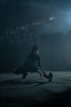 An athletic woman in a hijab performing stretching exercises indoors with a misty background effect.