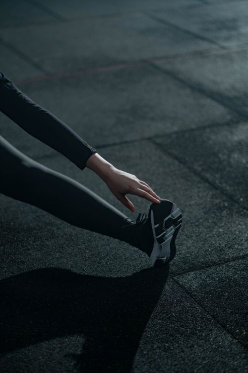 Free A person in activewear performing a stretching exercise indoors on a gym floor. Stock Photo