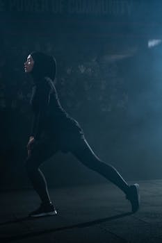 Muslim woman in activewear stretching in a moody, atmospheric gym setting.