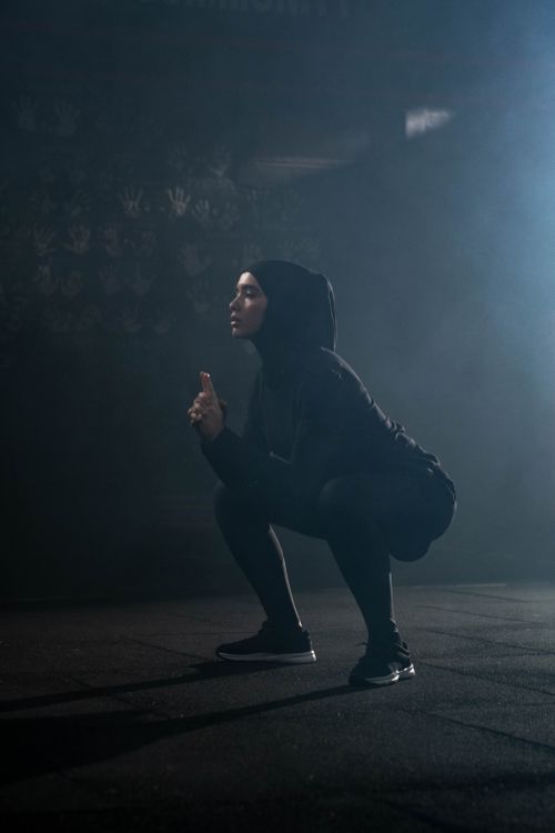 Free A woman wearing a hijab performs a squat in a gym with a smoky background. Indoors, focused on fitness. Stock Photo