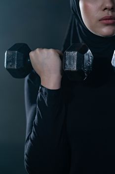 Close-up of a woman in hijab lifting a dumbbell, showcasing fitness and strength indoors.