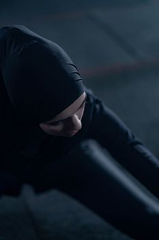 A Muslim woman wearing a hijab stretches during an evening workout session, captured with selective focus.