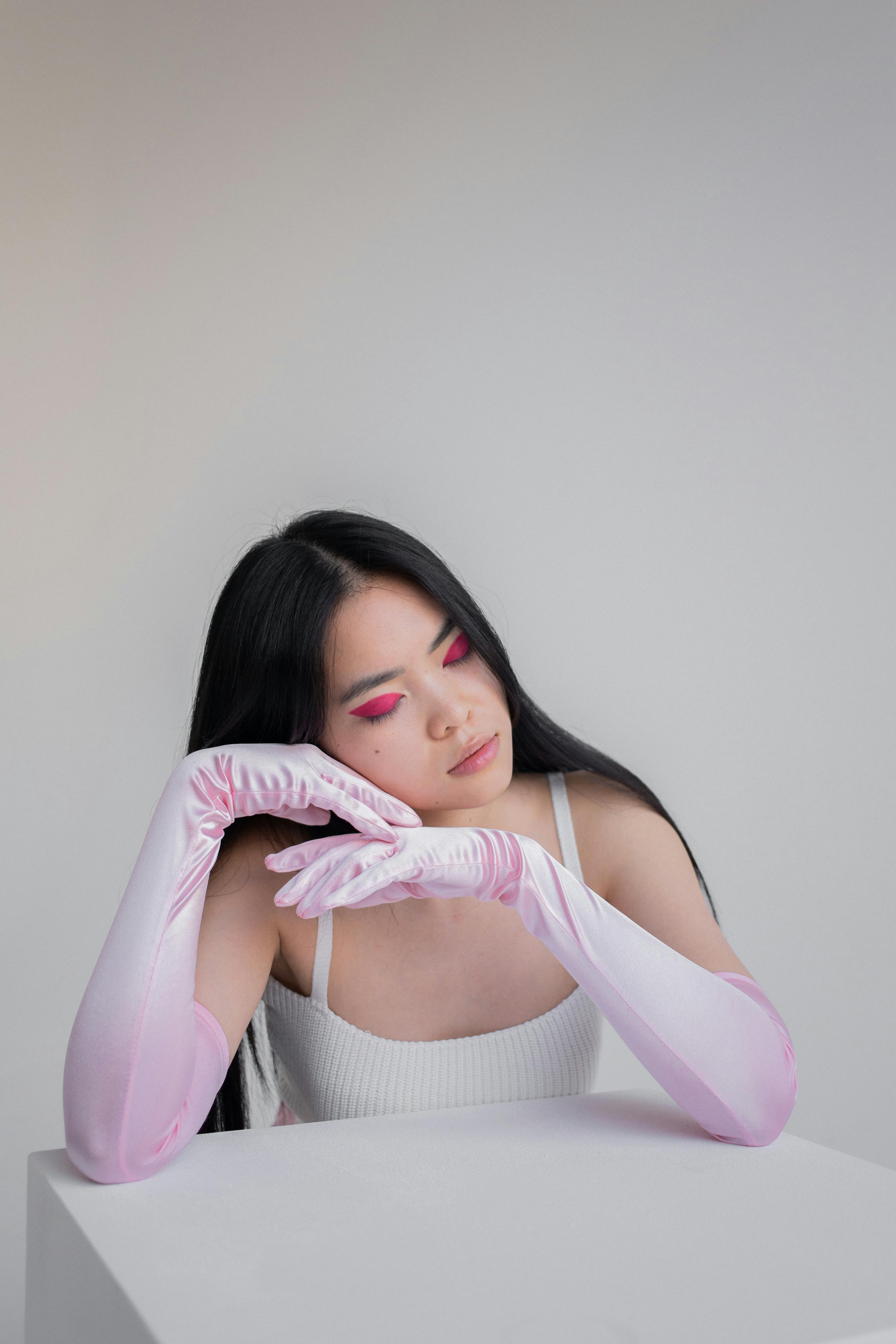 Young woman in pink gloves with eyes closed, posing in a minimalist indoor setting.