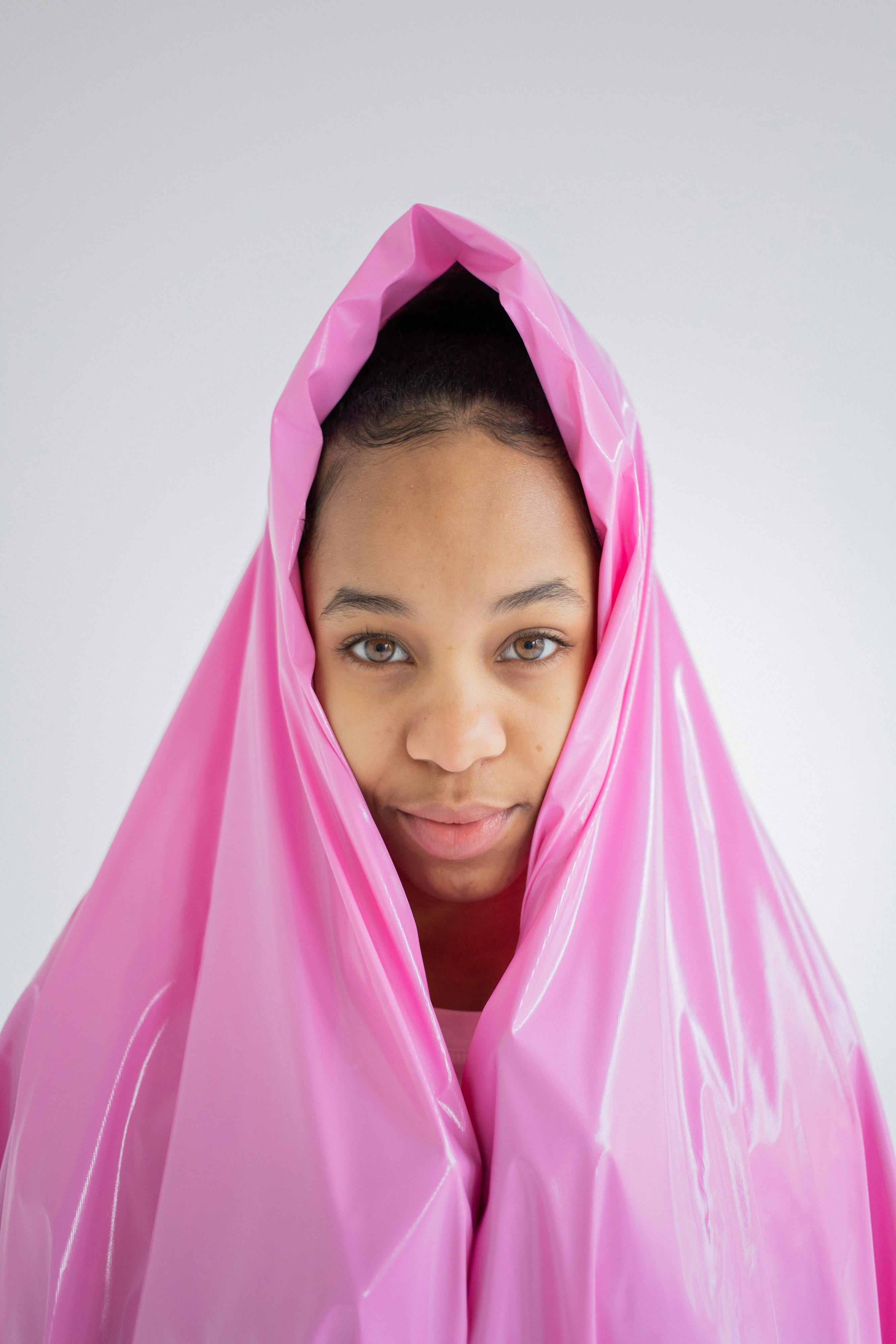 Stylish portrait of an African woman wrapped in pink plastic against a neutral background.
