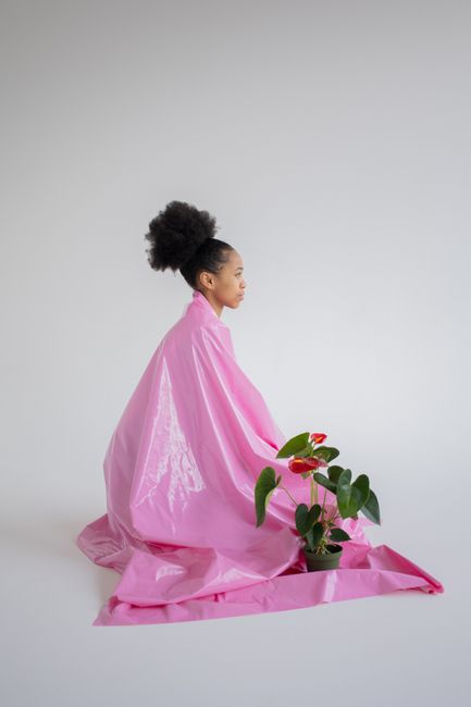 Creative portrait of a woman wrapped in pink fabric with an anthurium plant beside her.