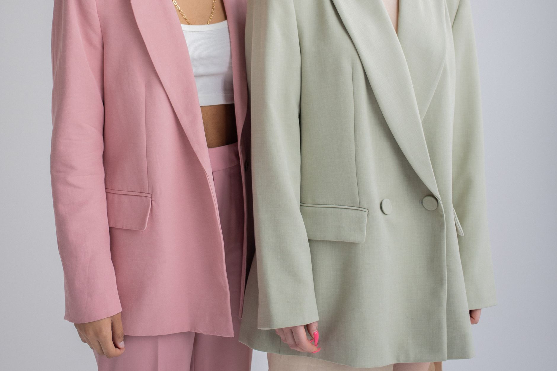 Crop unrecognizable female models wearing oversize stylish outfits standing close against gray background in studio