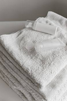 Stack of white towels with clean beauty products arranged on a smooth surface.