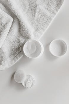 Top view of skincare products and towel on a white surface, showcasing minimalism.