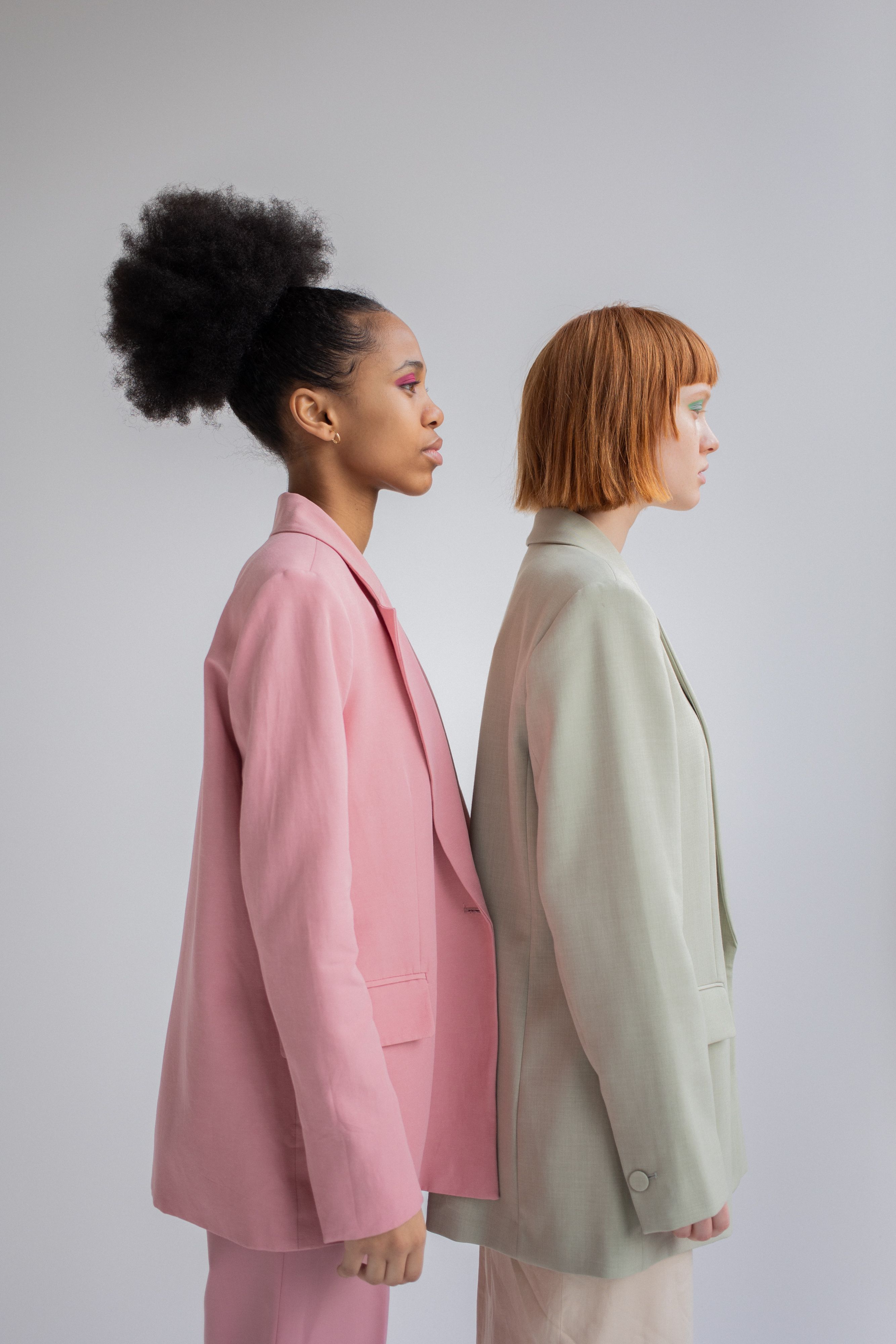 Duas jovens em blazers pastel, lado a lado, exibindo moda moderna.