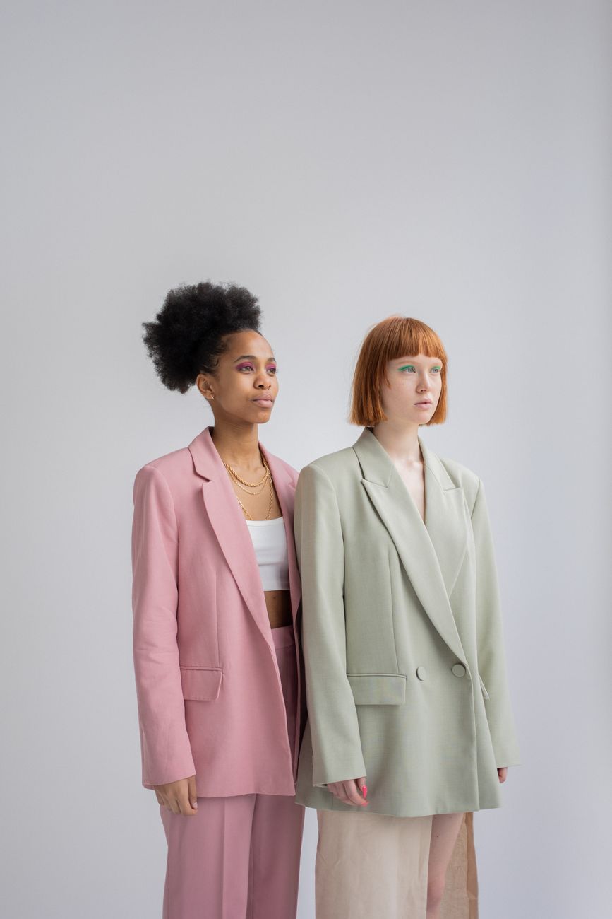 Duas mulheres em blazers elegantes posando com confiança em um estúdio.