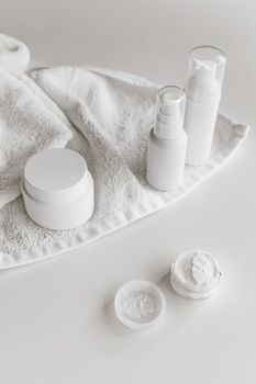 White cosmetics bottles and containers on a towel in minimal lighting.