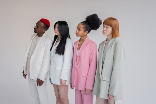 Multiethnic female models and man wearing elegant outfits standing in line against gray background and looking away with attention