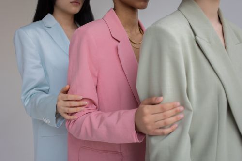 Free Side view of crop anonymous multiethnic female models wearing classy blazers in different pastel colors holding each others shoulders against gray background Stock Photo