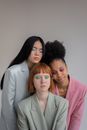 Peaceful delicate diverse female models with closed eyes in trendy blazers with colorful eyeshadows against gray background