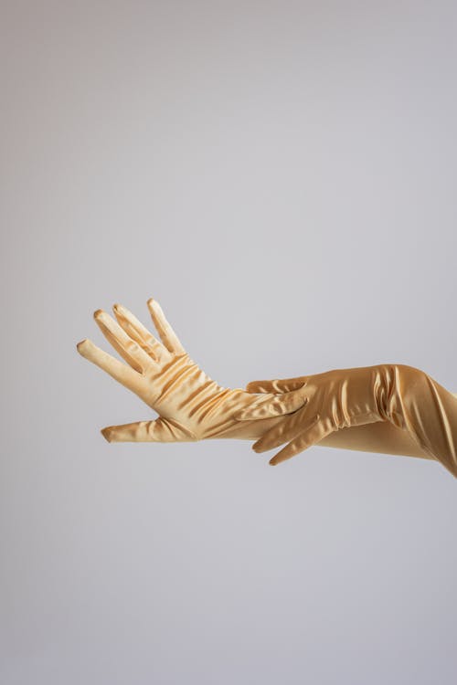 Crop anonymous female gently touching hands in silk vintage gloves in studio against gray background