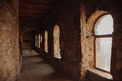 Free Explore the timeless beauty of an ancient stone corridor with arched windows and textured walls. Stock Photo