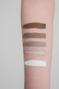 Crop anonymous female showing hand with samples of different colors painted on bare skin on gray background