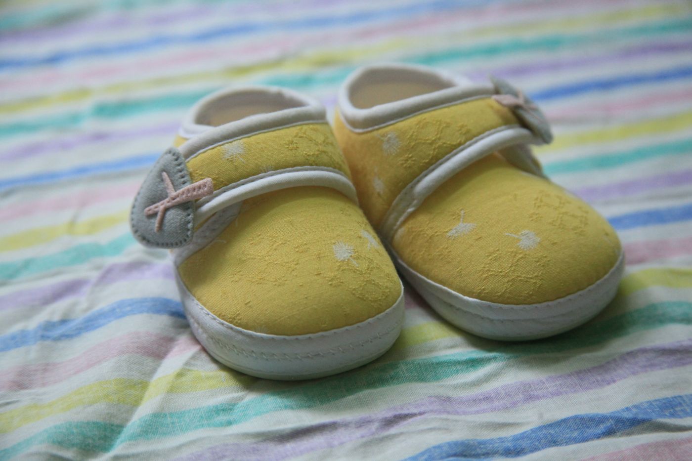 Yellow baby shoes resting on a colorful striped blanket