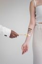 Crop unrecognizable female in white clothes standing while black male drawing on hand of woman on white background