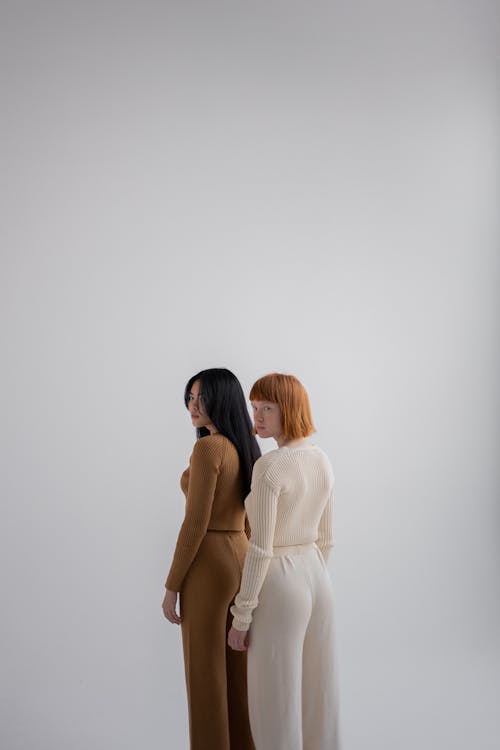 Young multiethnic women wearing casual outfits of different colors standing together in similar poses on white background while looking at camera over shoulder